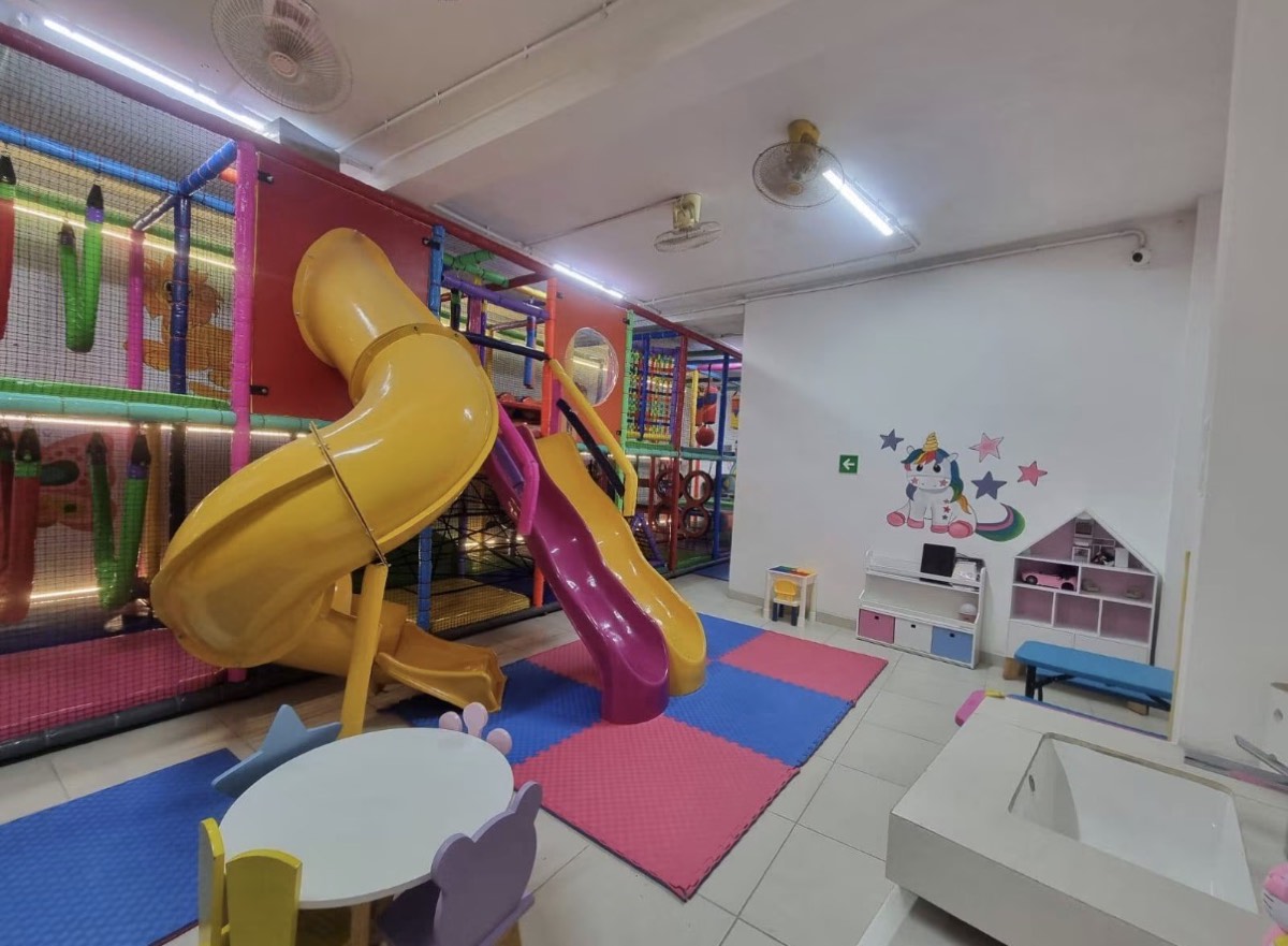 Área de juegos con toboganes, mesas infantiles y mural de unicornio